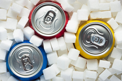Unhealthy food concept - sugar in carbonated drinks. Sugar cubes as background and canned drinks